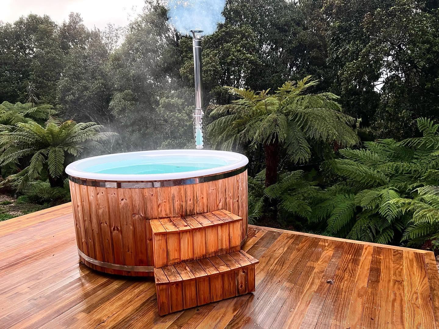 Steaming outdoor cedar spa on a deck with bush ranges at dusk