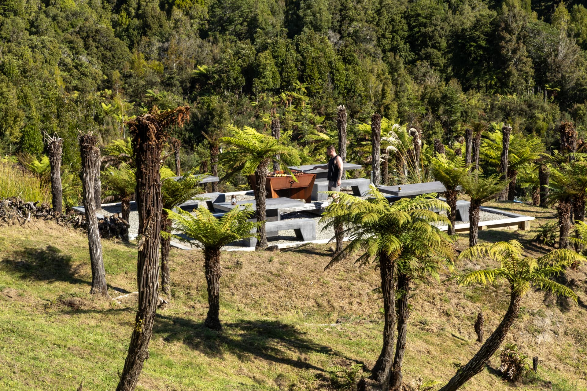 Chef grilling at the outdoor cooking area surrounded by tree ferns