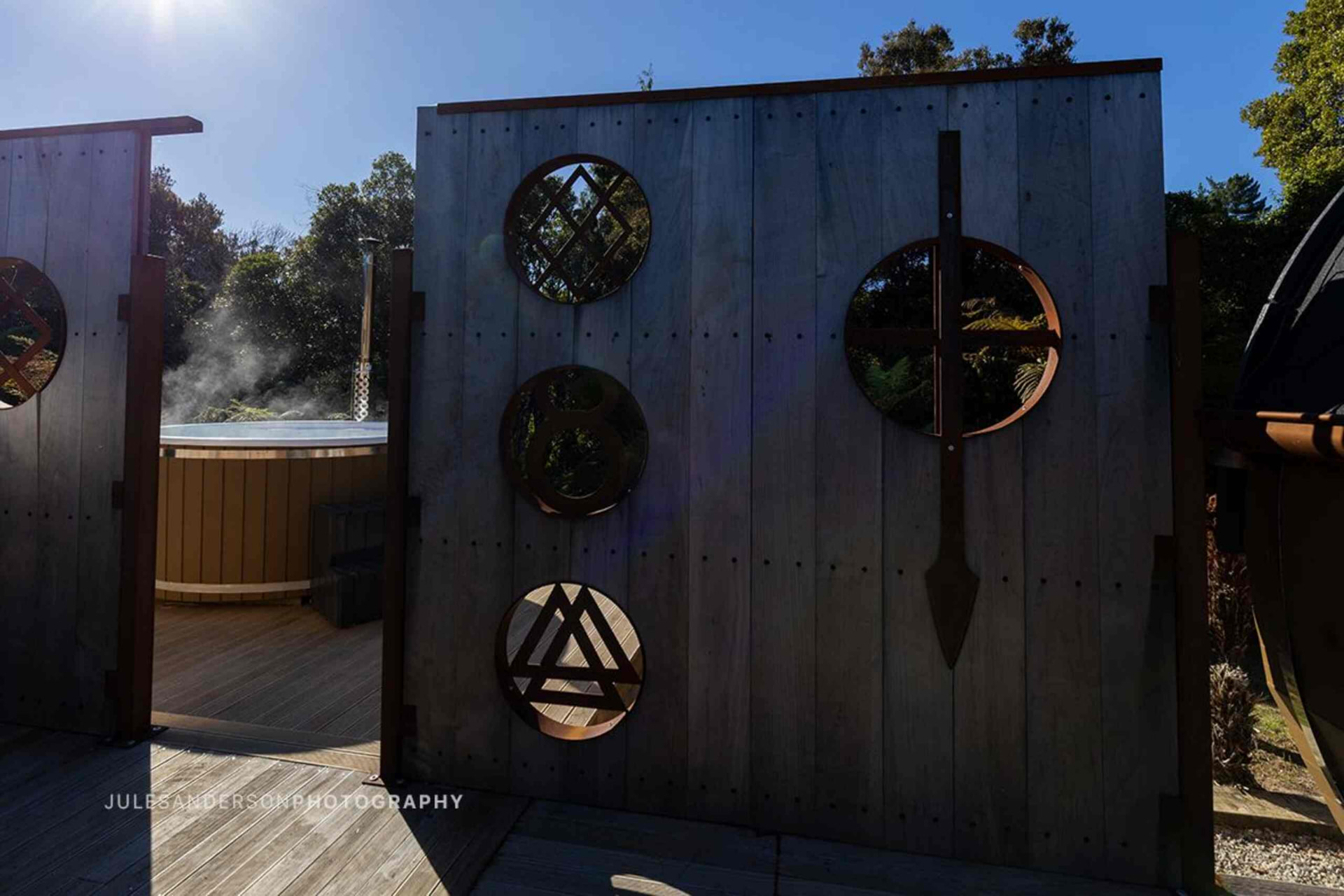 Timber privacy gate with Norse symbols opening to a steaming outdoor spa on a deck