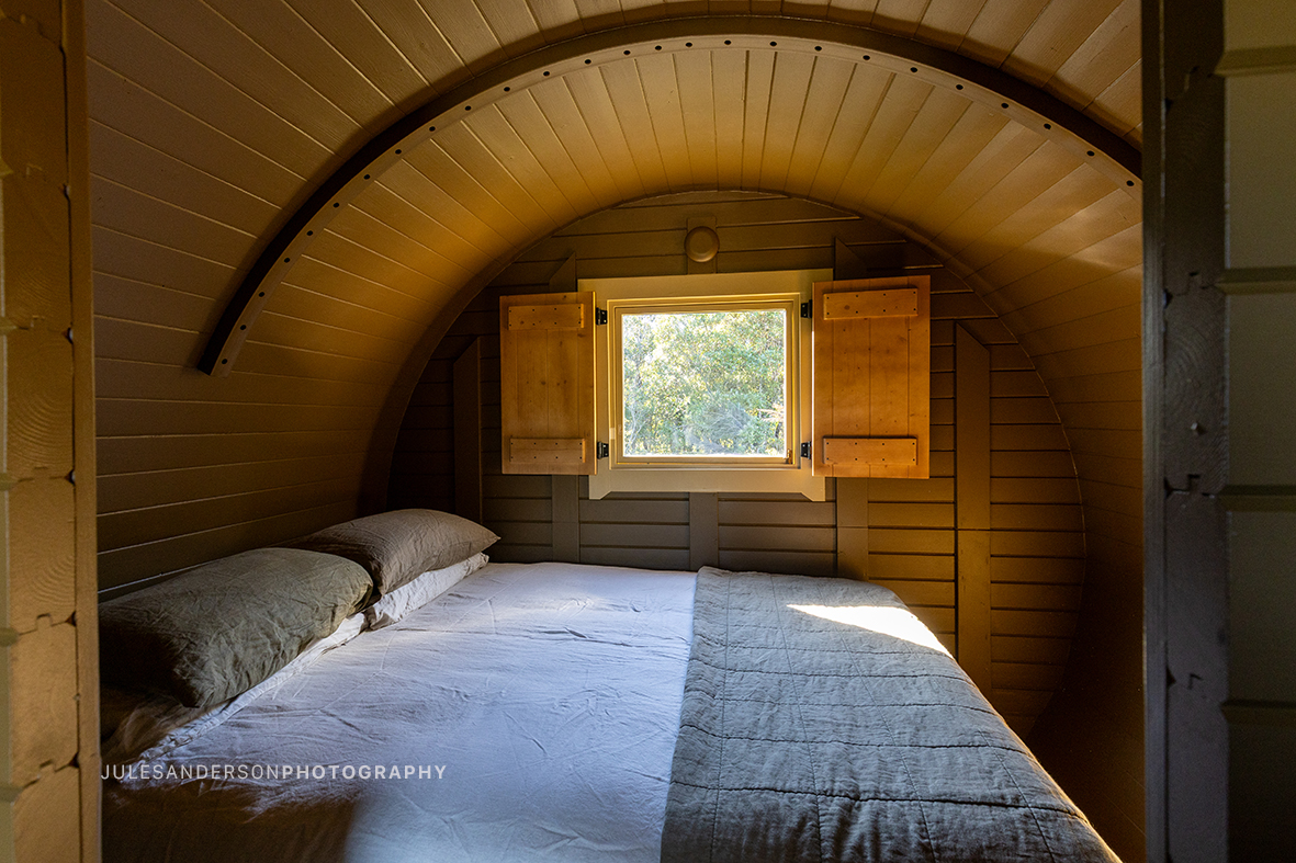 Cosy double bed inside the Odin barrel cabin with a shuttered window looking into the forest