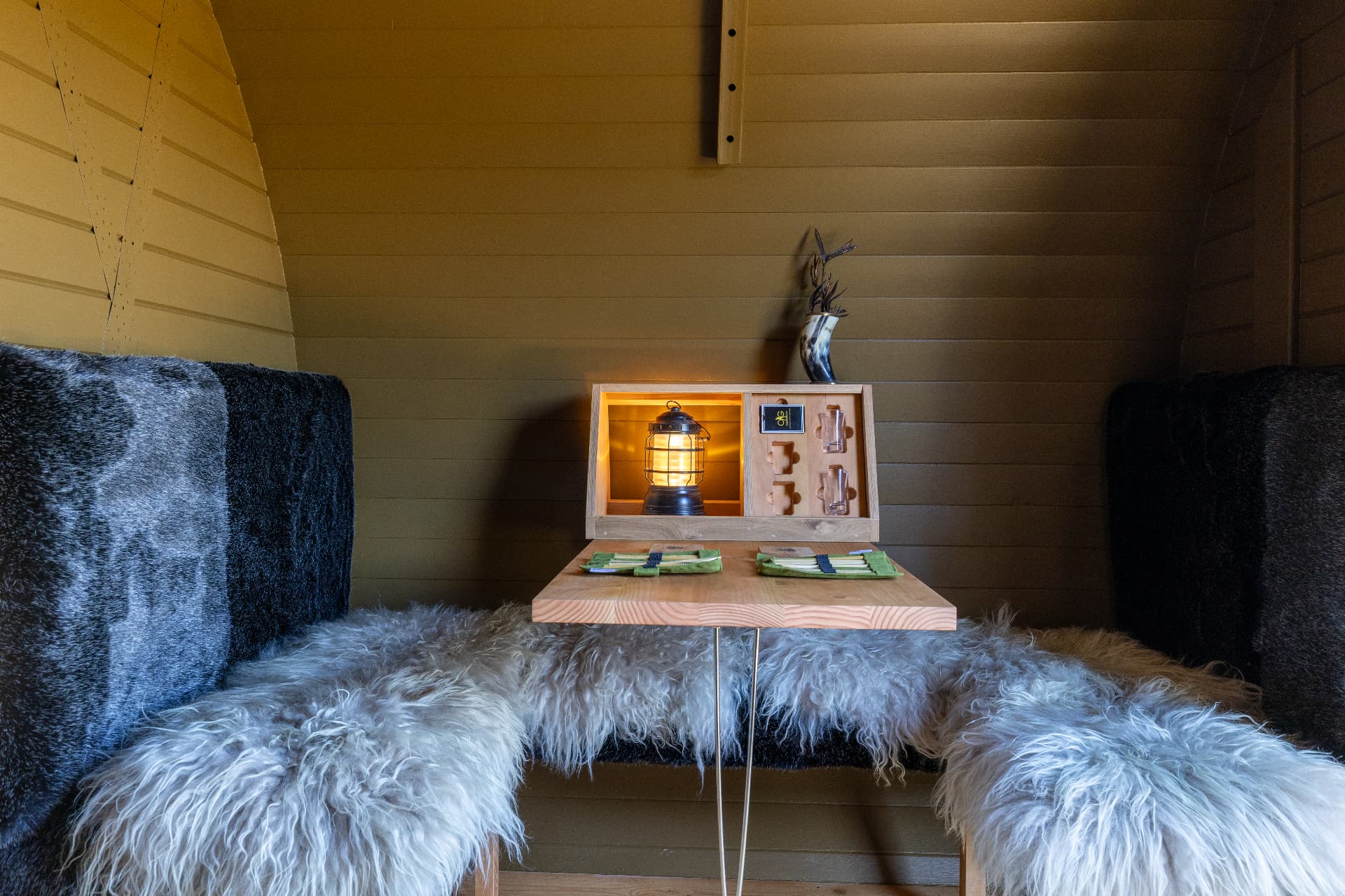Barrel cabin dining nook with sheepskin seating and a lit lantern